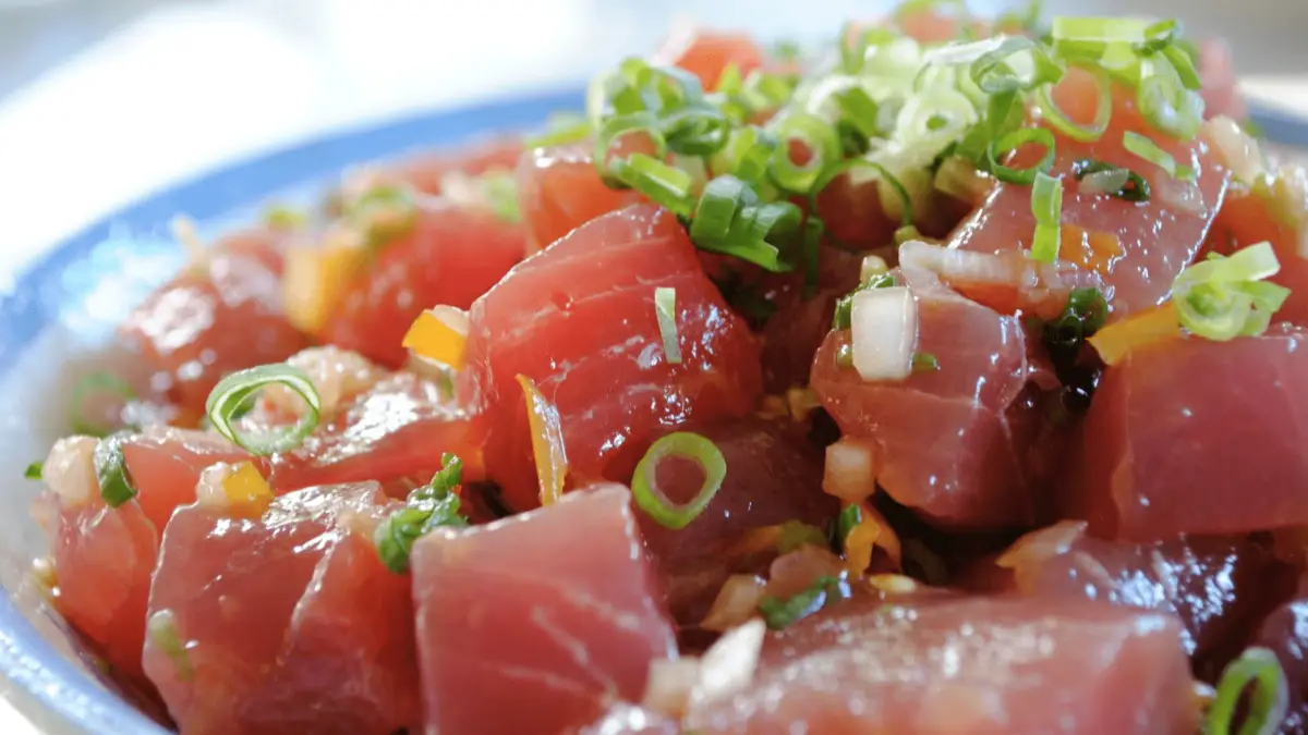 Close-up shot of a bowl of Poke, a staple in Foods That Define Hawaiian Culture, consisting of raw, cubed fish (likely tuna) mixed with chopped green onions and garnished with sliced green onions on top. The vibrant colors and freshness are clearly visible, showcasing the best of Hawaiian seafood.