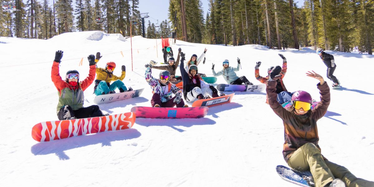 Women snowboarders sitting on mountain with hands raised