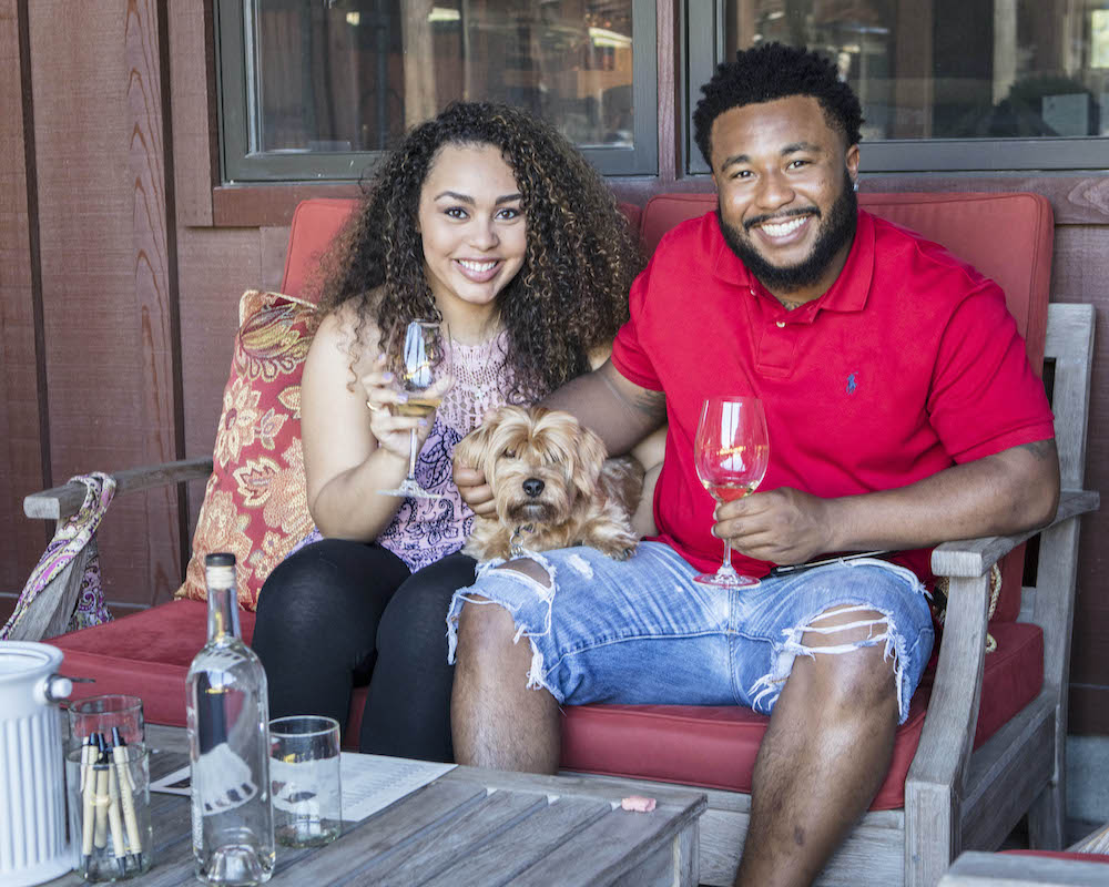 Couple sits with their dog and wine glasses at Pawsport in Napa Valley.