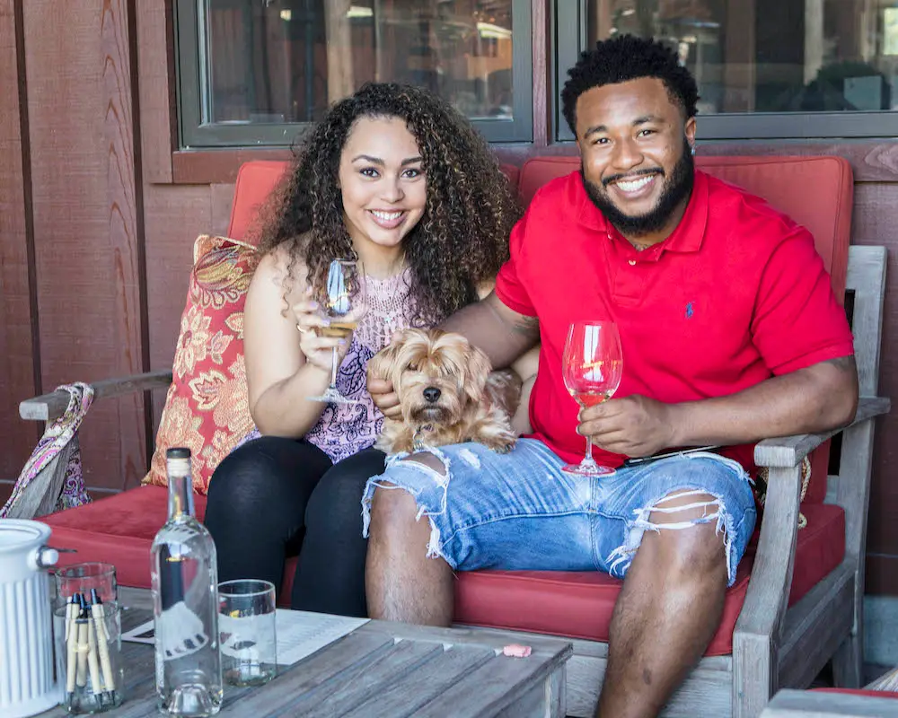 Couple sits with their dog and wine glasses at Pawsport in Napa Valley.