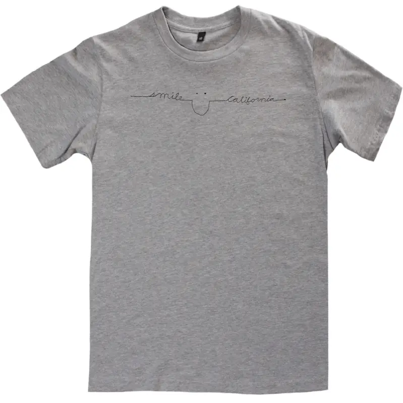 A gray T-shirt with minimalistic design features the words "smile" and "California" separated by a simple line drawing of a smiley face, part of our exclusive Smile Collection.