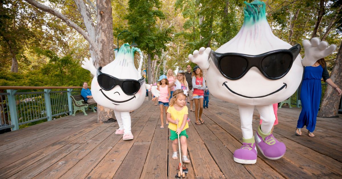 Girl walks next to two giant Garlic mascots at Gilroy Gardens Theme Park in the South Bay
