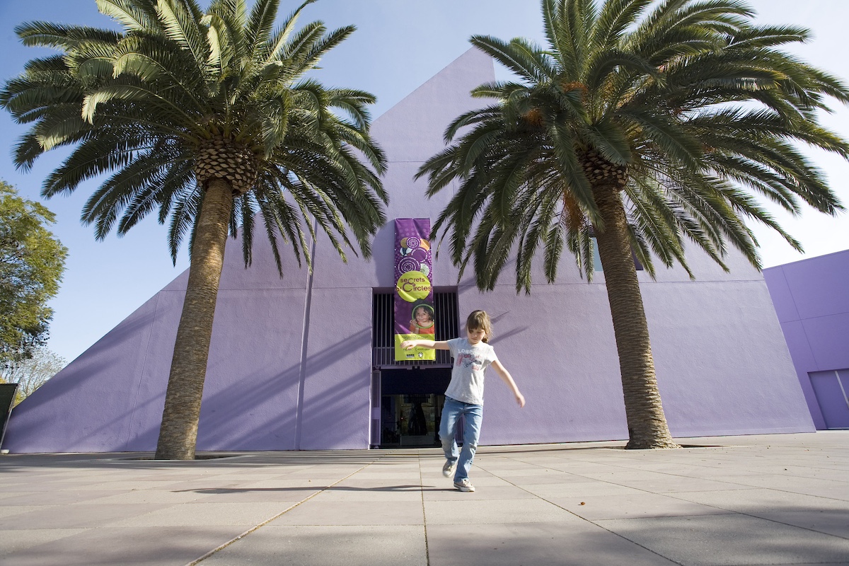 Child balances on one foot in front of San Jose's Children's Discovery Museum