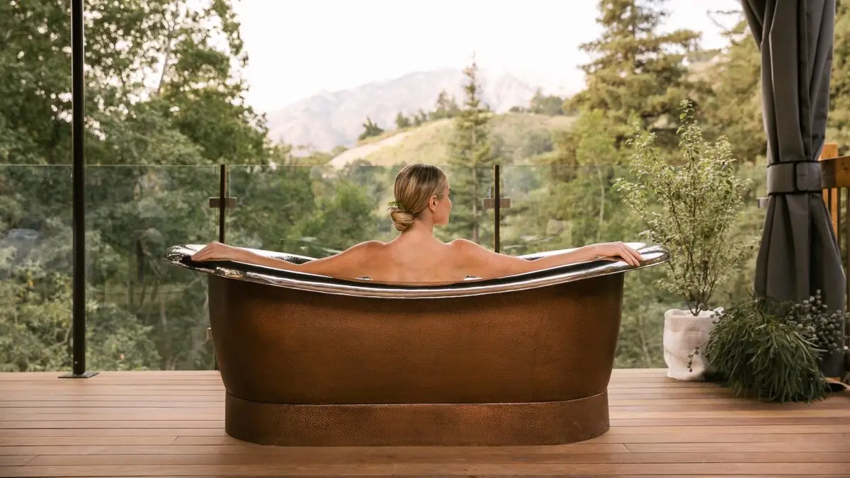 Woman sits in spa bathtub overlooking the hills of Monterey Peninsula from her hotel room at Ventana in Big Sur, California