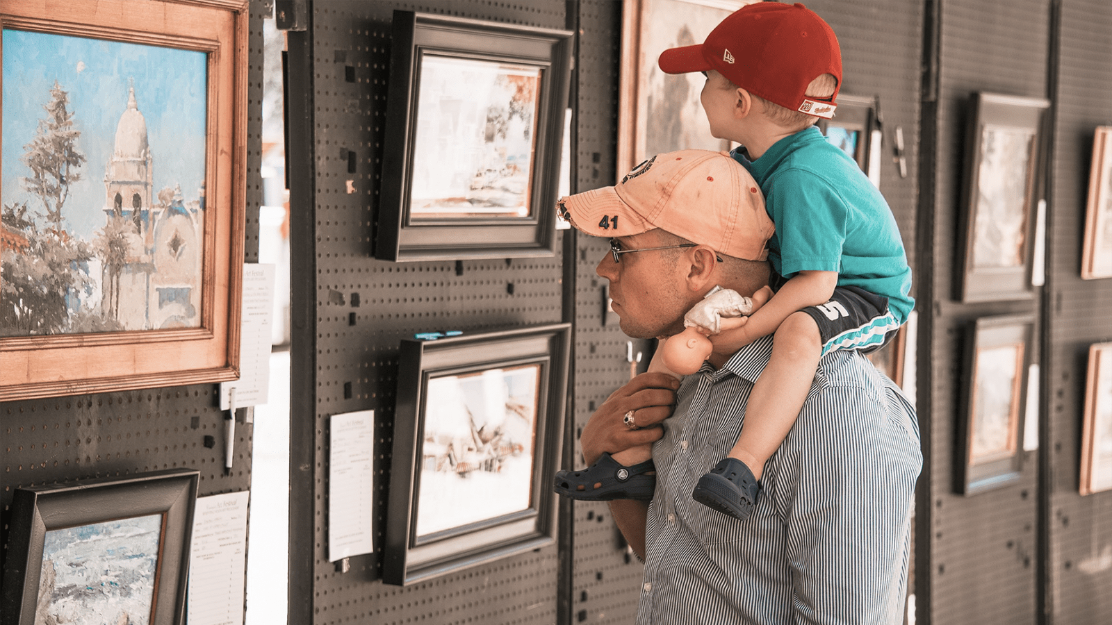 Child sits on man's shoulders looking at painting at Carmel Art Festival in Carmel-by-the-sea, California.