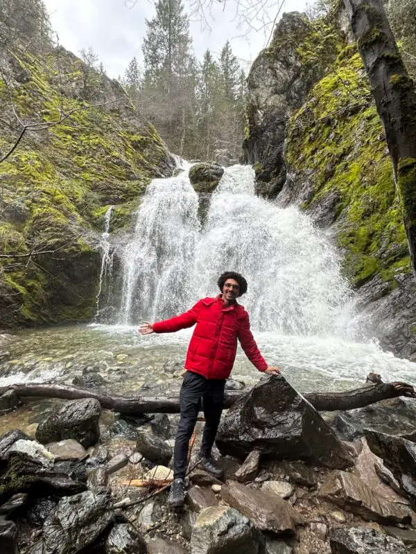 Jordan Reid stands in front of large waterfall at Faery Falls hike in Mount Shasta, California