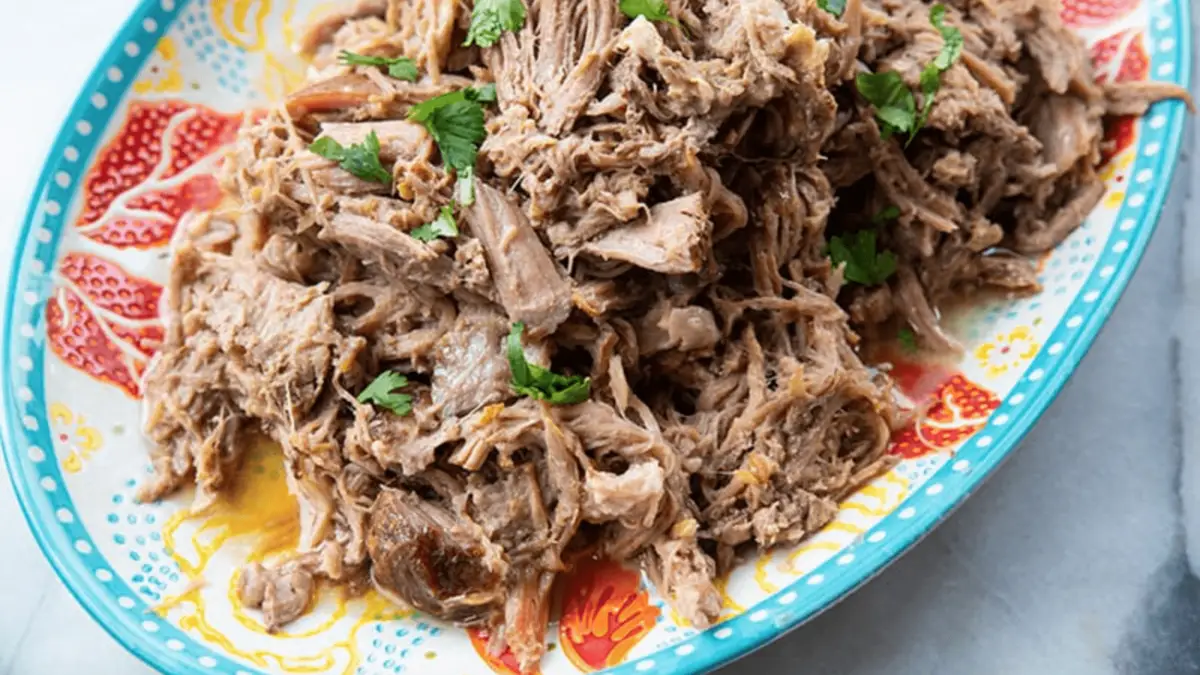 A brightly colored plate holds a generous serving of shredded pork garnished with chopped parsley. The pork, reminiscent of traditional Hawaiian luau history, appears tender and moist, with pieces slightly pulled apart, showcasing a succulent texture.