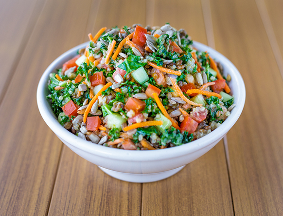 A white bowl filled with a colorful salad of chopped tomatoes, cucumbers, carrots, kale, and grains sits on a wooden surface. It's no wonder why this vibrant dish is considered the Best Lunch in Marin!