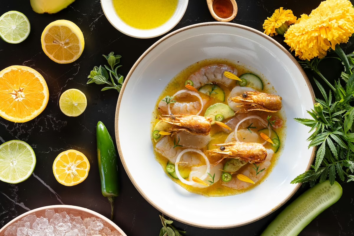 An aerial shot of a bowl with seafood in a sauce, and many ingredients are displayed around.
