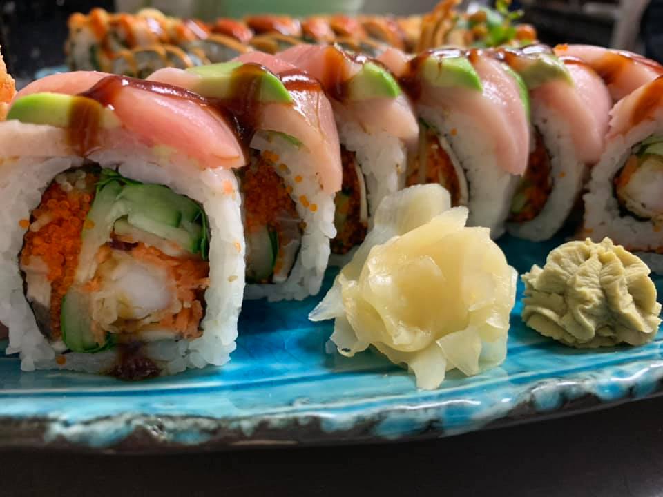 A close-up of the best sushi in Mendocino, featuring intricately arranged sushi rolls filled with ingredients like cucumber, fish roe, and shrimp, topped with slices of avocado and fish. The platter also includes a serving of pickled ginger and wasabi.