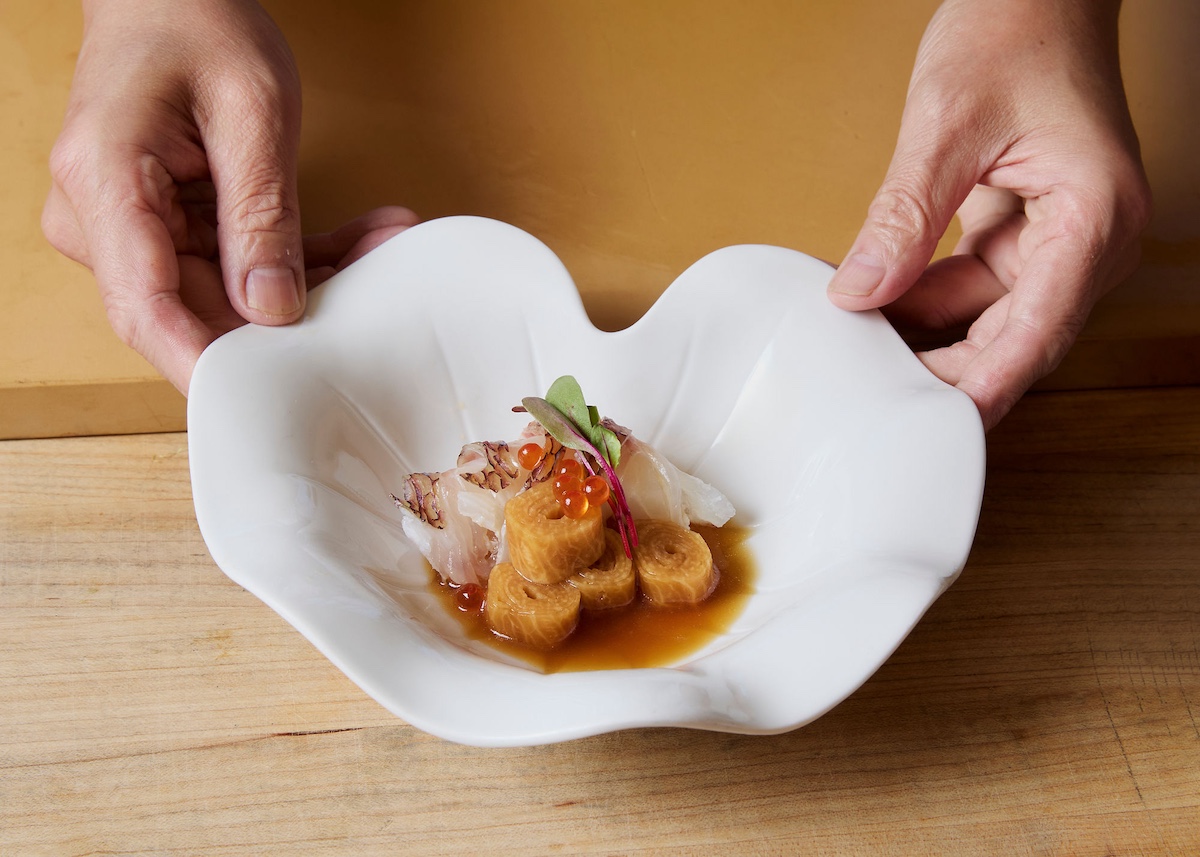 A white plate being held with some sushi in a brownish sauce.