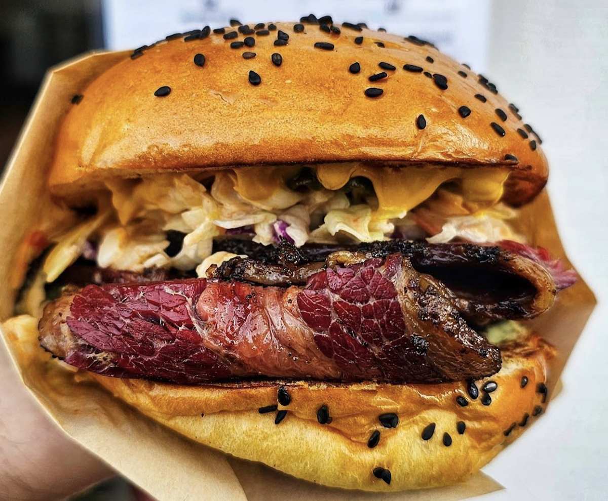 Close-up of a juicy sandwich with a golden bun topped with black sesame seeds. The filling features thick slices of pastrami, coleslaw, and a creamy dressing, all nestled in the soft bun. The sandwich looks fresh, flavorful, and appetizing—definitely one to try if you're wondering where to eat in the Bay Area.