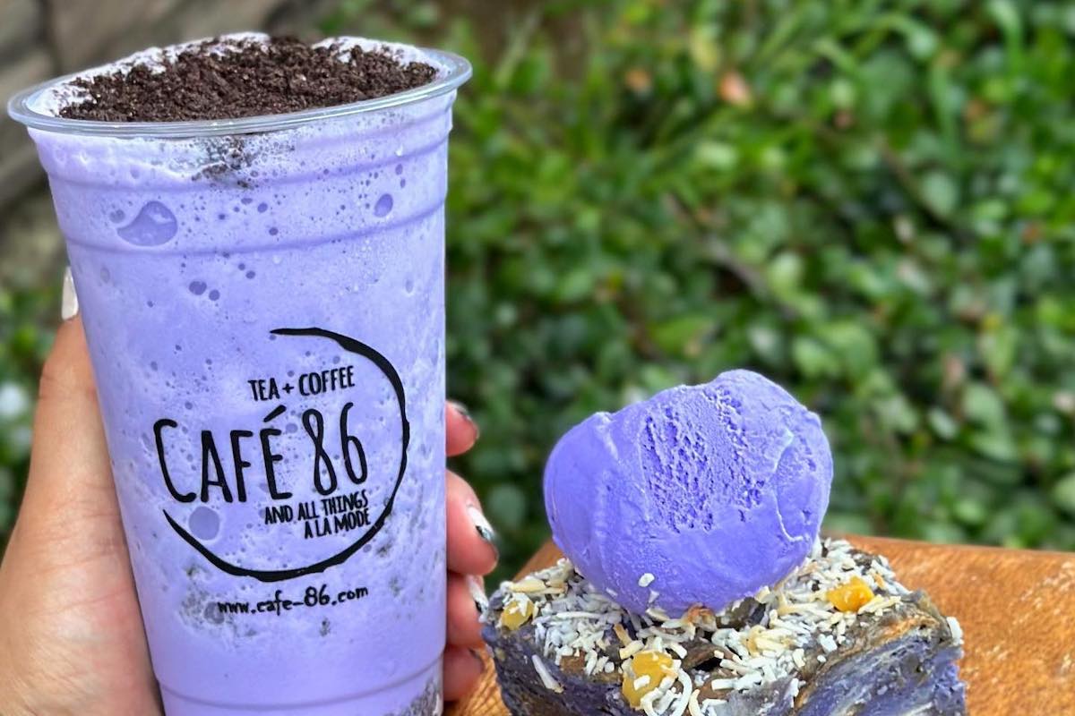 Photo of someone holding a blended purple ube drink with crushed Oreos and a purple ube dessert next to them.