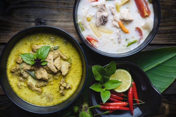 Green curry pork, chicken coconut soup or Thai in names "Kaeng Keaw Whan" and Tom Kha Gai. Top view on wooden background.