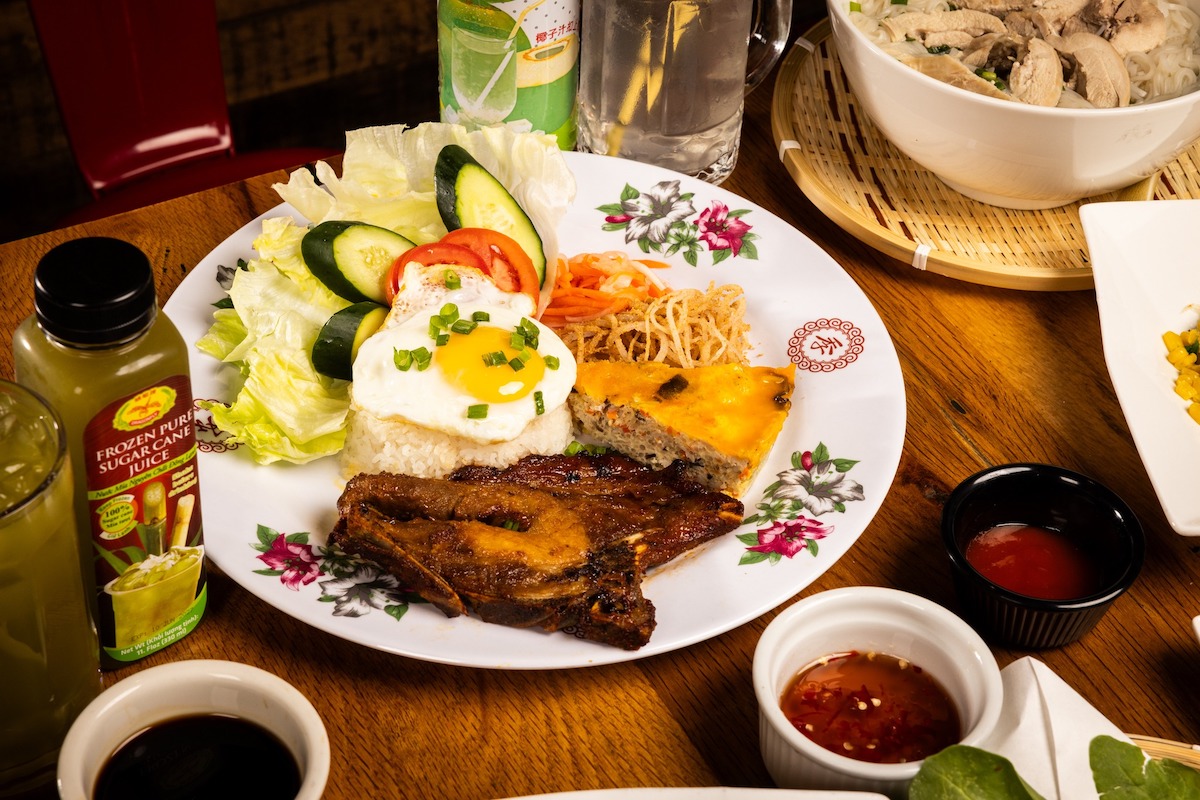 A plate of Vietnamese food, including an egg, meat and some veggies with bowls of sauce around.