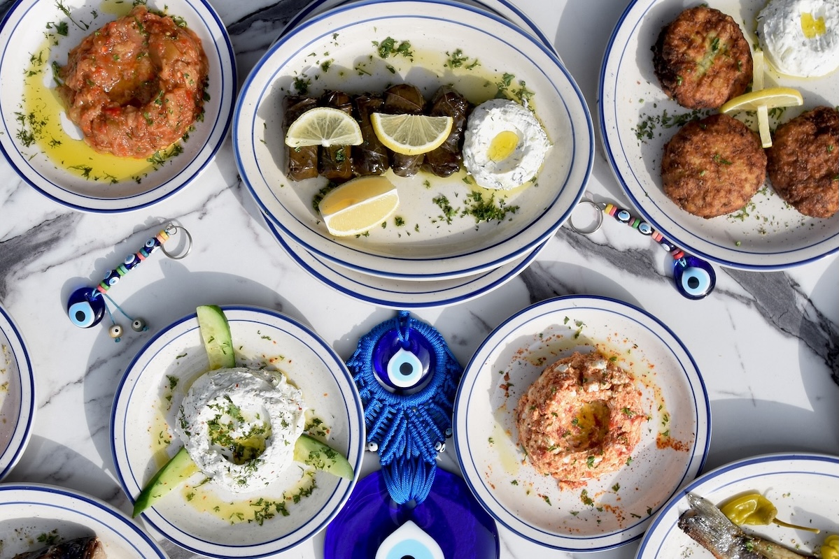 Plates of Greek food and dips with evil eyes surrounding the plates.