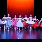 Dancers in the Nutcracker stand on a stage to bow, with a red backdrop.