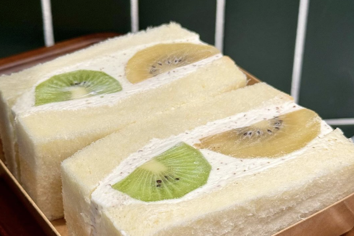 A sandwich with white bread, green and gold kiwis and whipped cream.