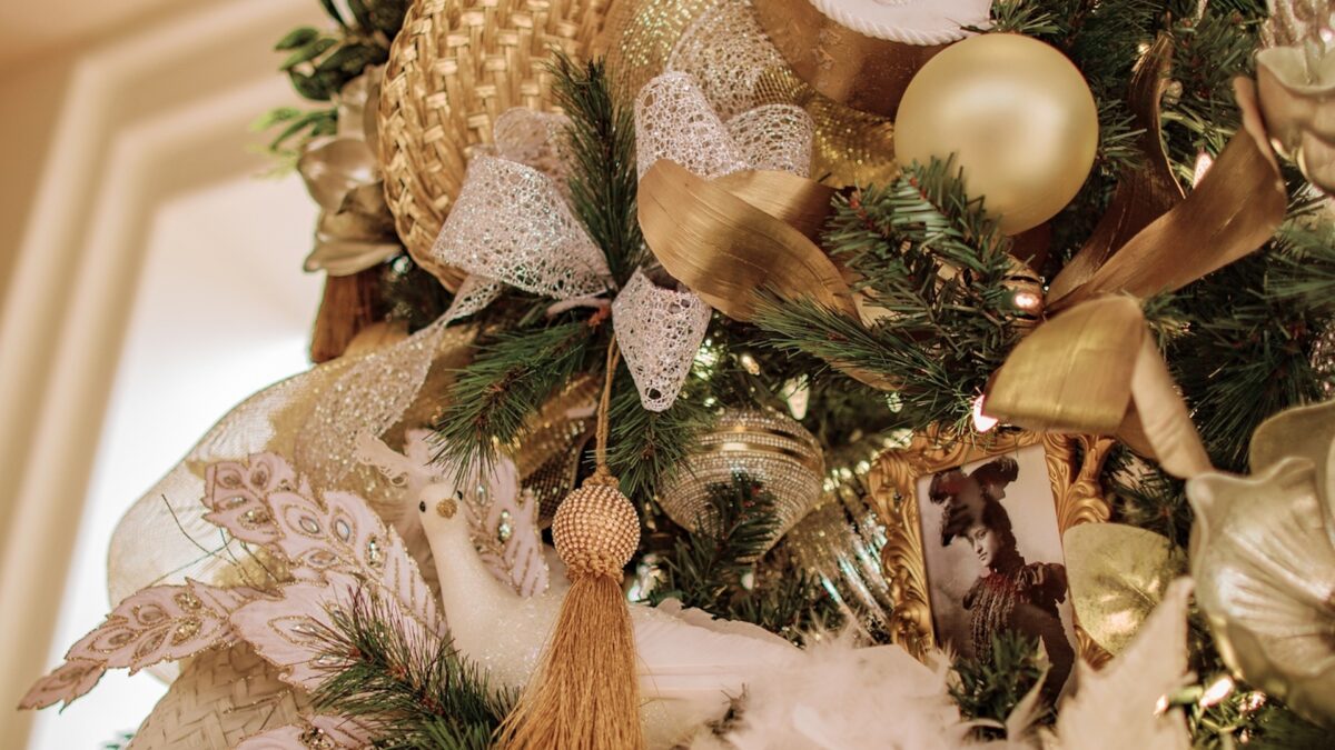 A close-up shot of decor on a Christmas tree, with gold ribbons, ornaments, lights and garland.