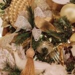 A close-up shot of decor on a Christmas tree, with gold ribbons, ornaments, lights and garland.