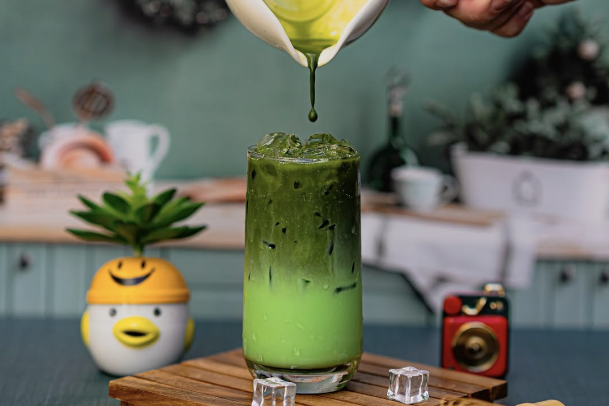 Someone pours matcha into a cup on a wooden board with a succulent next to it.