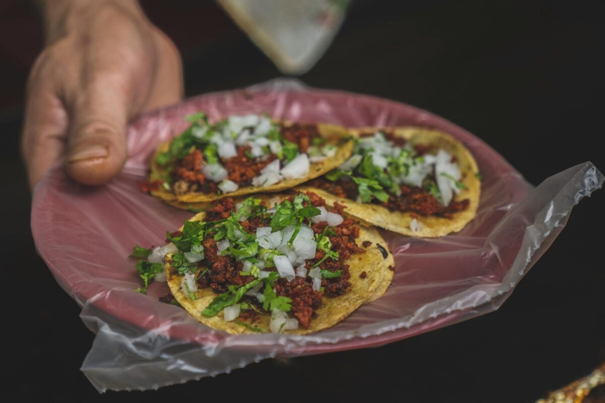 Someone holds a plate of tacos with meat, onions and chopped green onions.