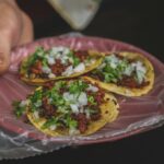 Someone holds a plate of tacos with meat, onions and chopped green onions.