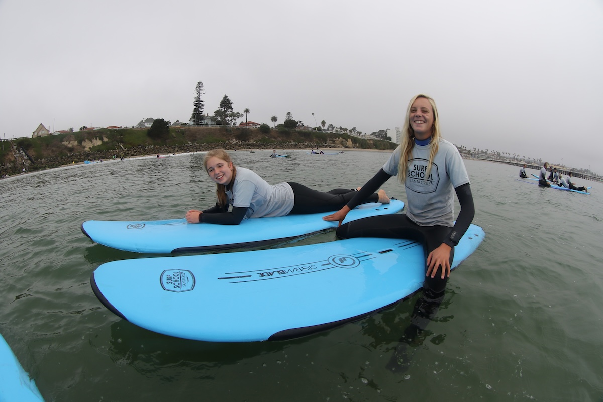 Two suit instructors wearing matching gray shirts each sit on a blue surfboard on the water.