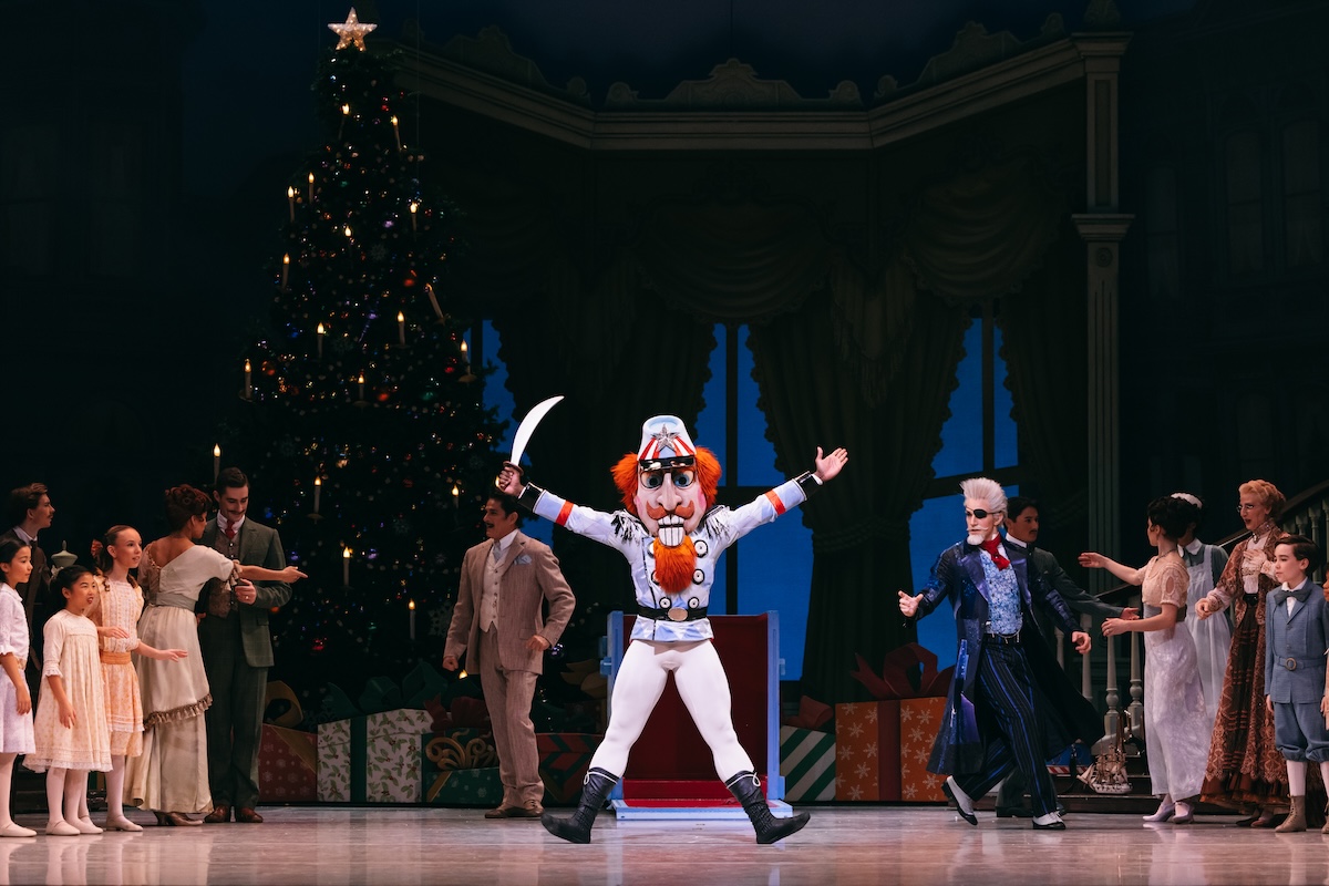 Ballet dancers onstage at San Francisco Ballet performing the Nutcracker. Lead dancer dressed as the Nutcracker stands in the middle with arms outstretch holding a sword.