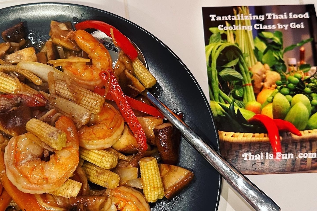 A plate of stir fry with shrimp and veggies and a pamphlet promoting a Thai food cooking class.