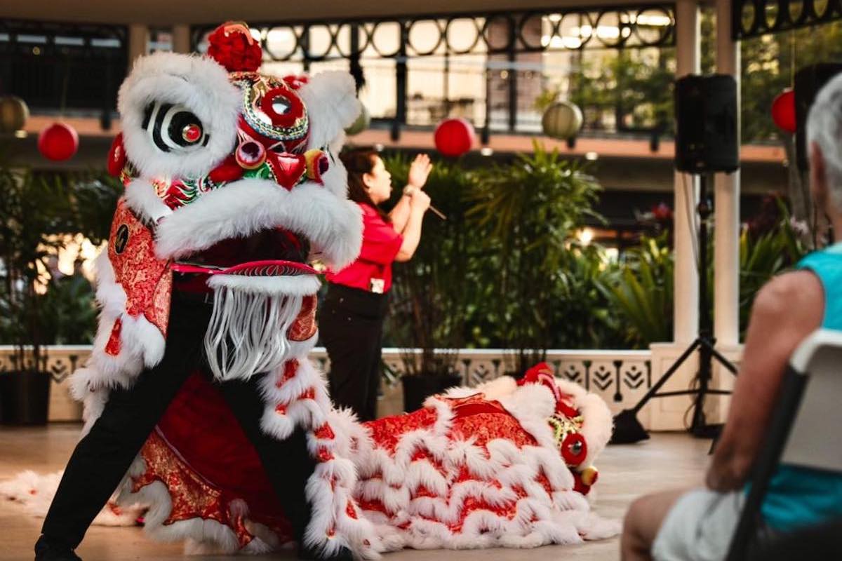 A red and white dragon dances in a dragon dance on a stage while people watch.