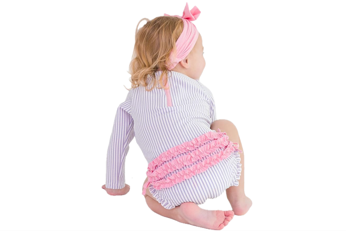 A little girl is wearing a pastel blue, one piece swim suit with a pink ruffle on the butt.