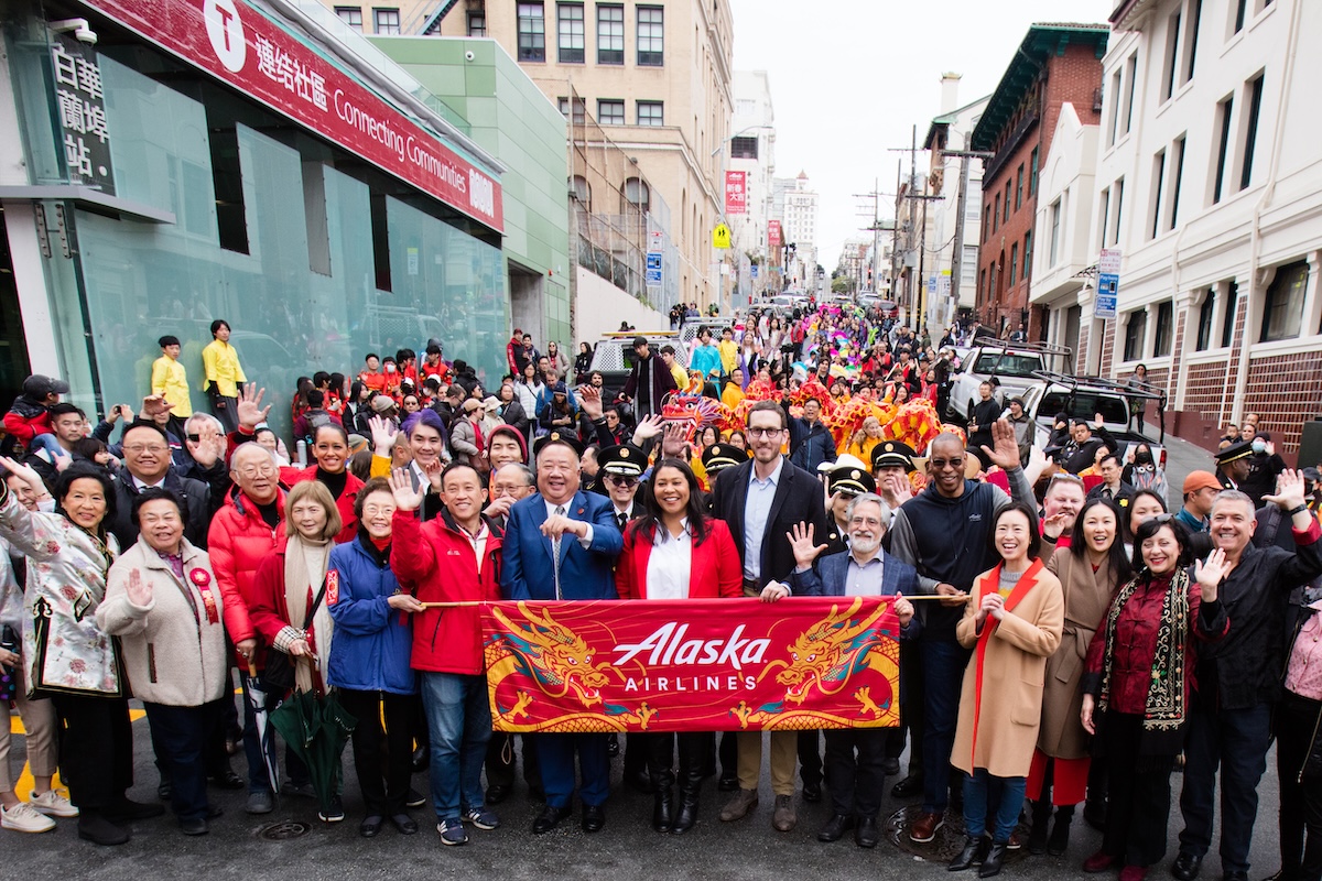 Group of famous San Franciscans stand with sign for Chinatown Flower Street Fair