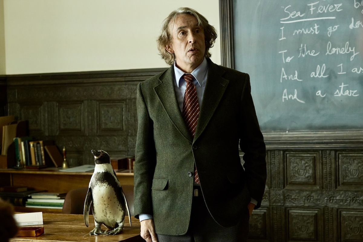 Film still of Steve Coogan standing next to an African penguin in a university setting.