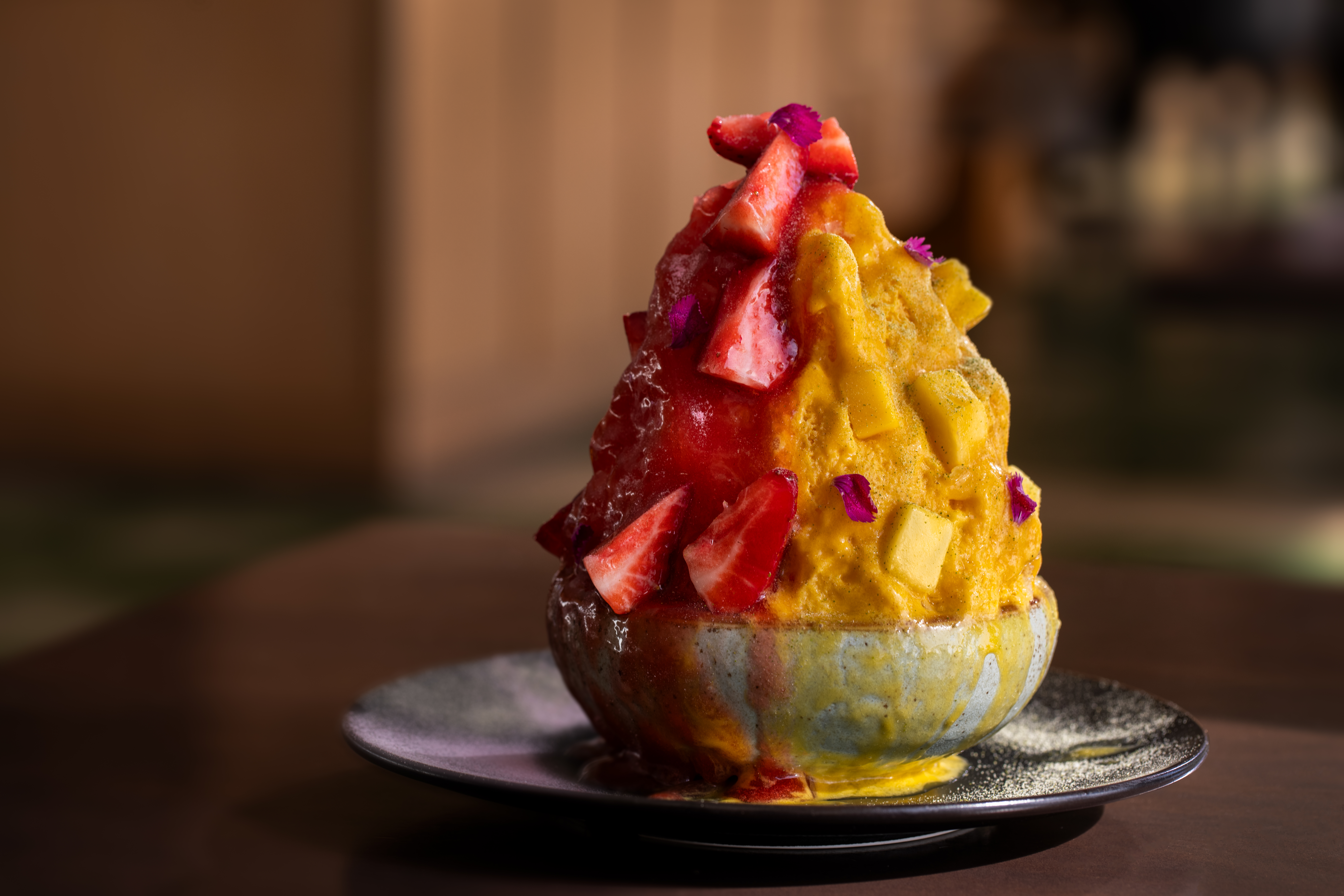 A bowl of shave ice, one half being pink and topped with strawberries, the other half being yellow and topped with mango.