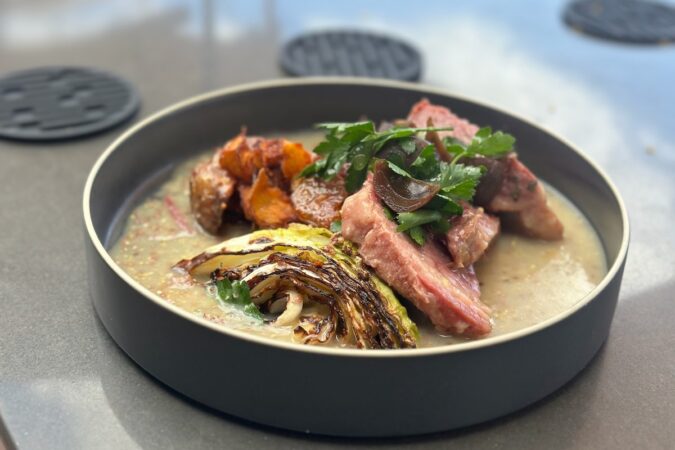 A bowl of sauce with meat, cooked cabbage, sweet potato and cilantro.