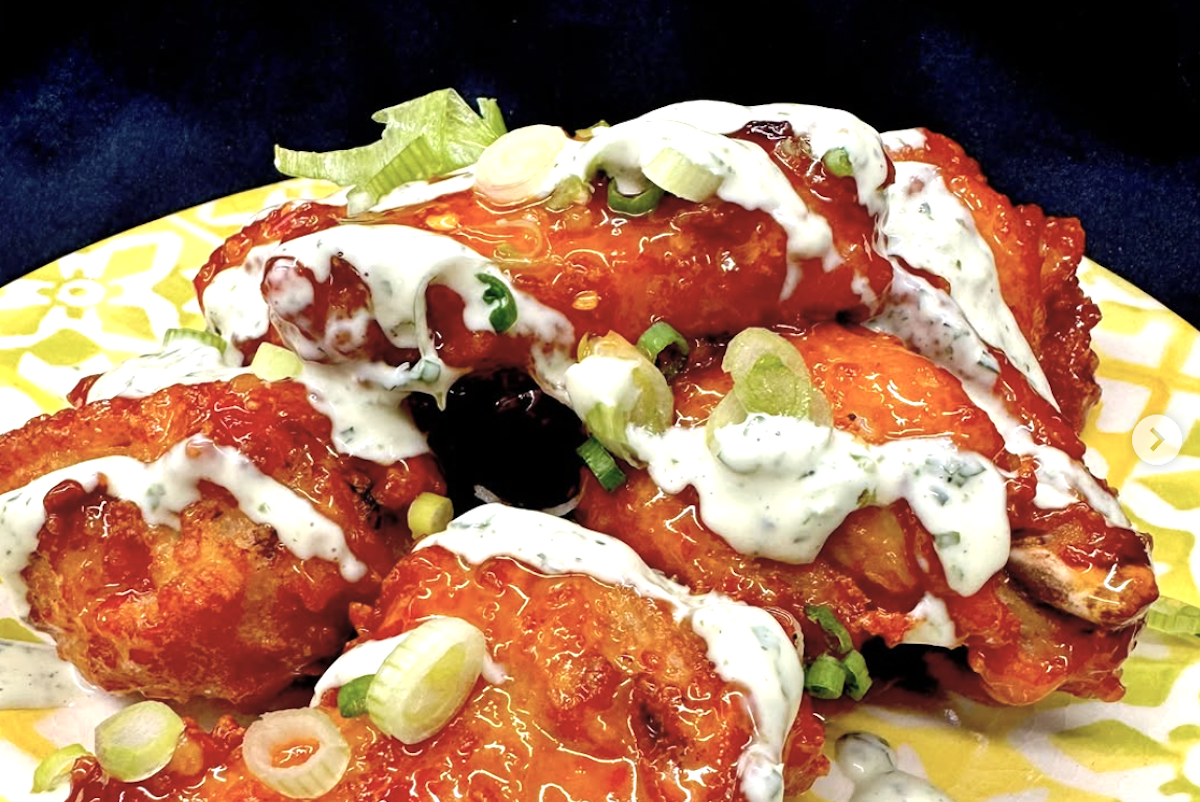 Bright orange battered and fried pieces of chicken, glazed in sauce and top with drizzles of a white sauce and some chopped green onion.