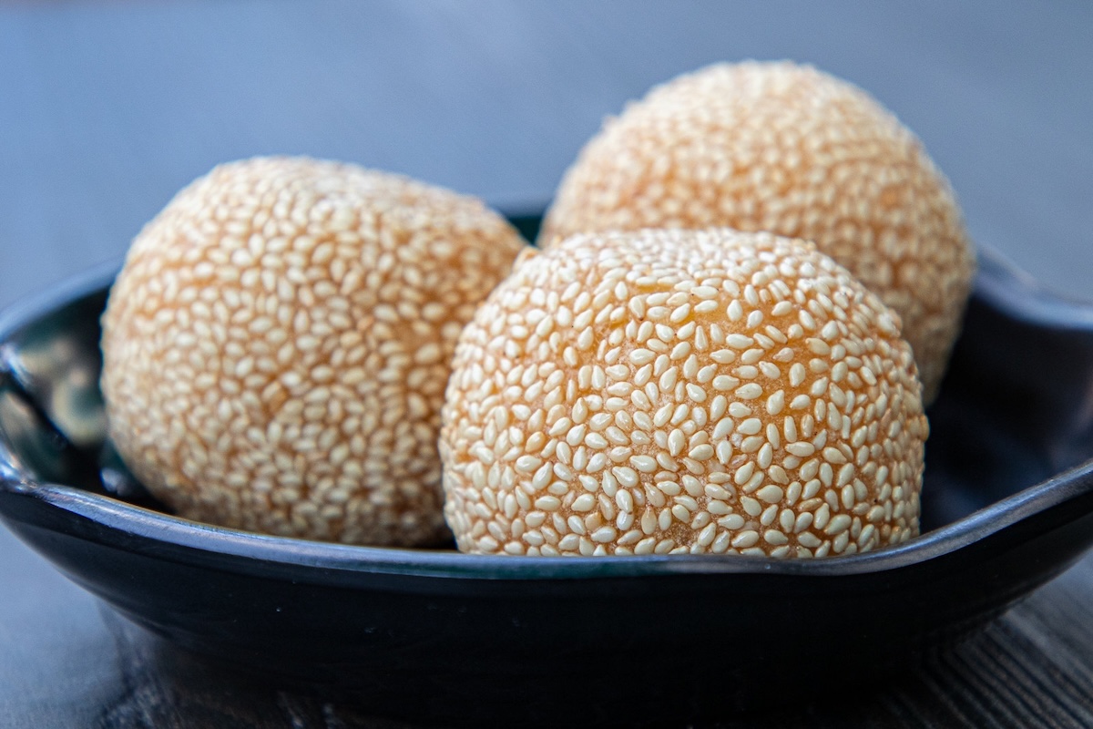 Three sesame balls sit on a black plate on top of a black wooden table.