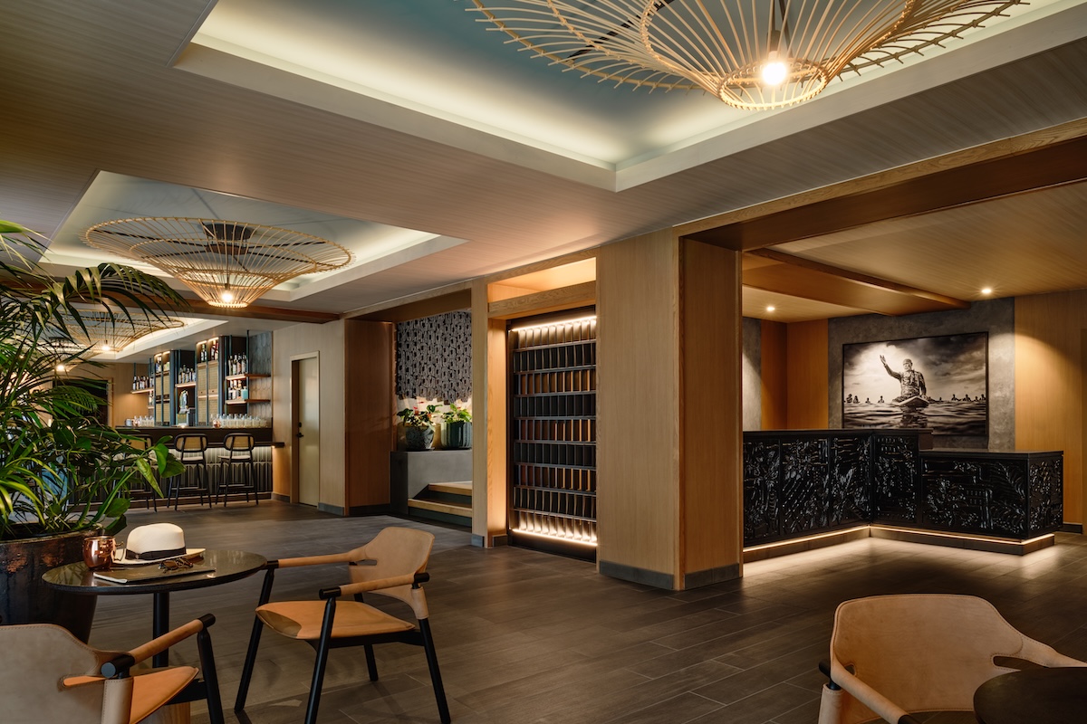 A hotel lobby with sultry, dim lighting leather seating, large wicker chandeliers, indoor palms and more.