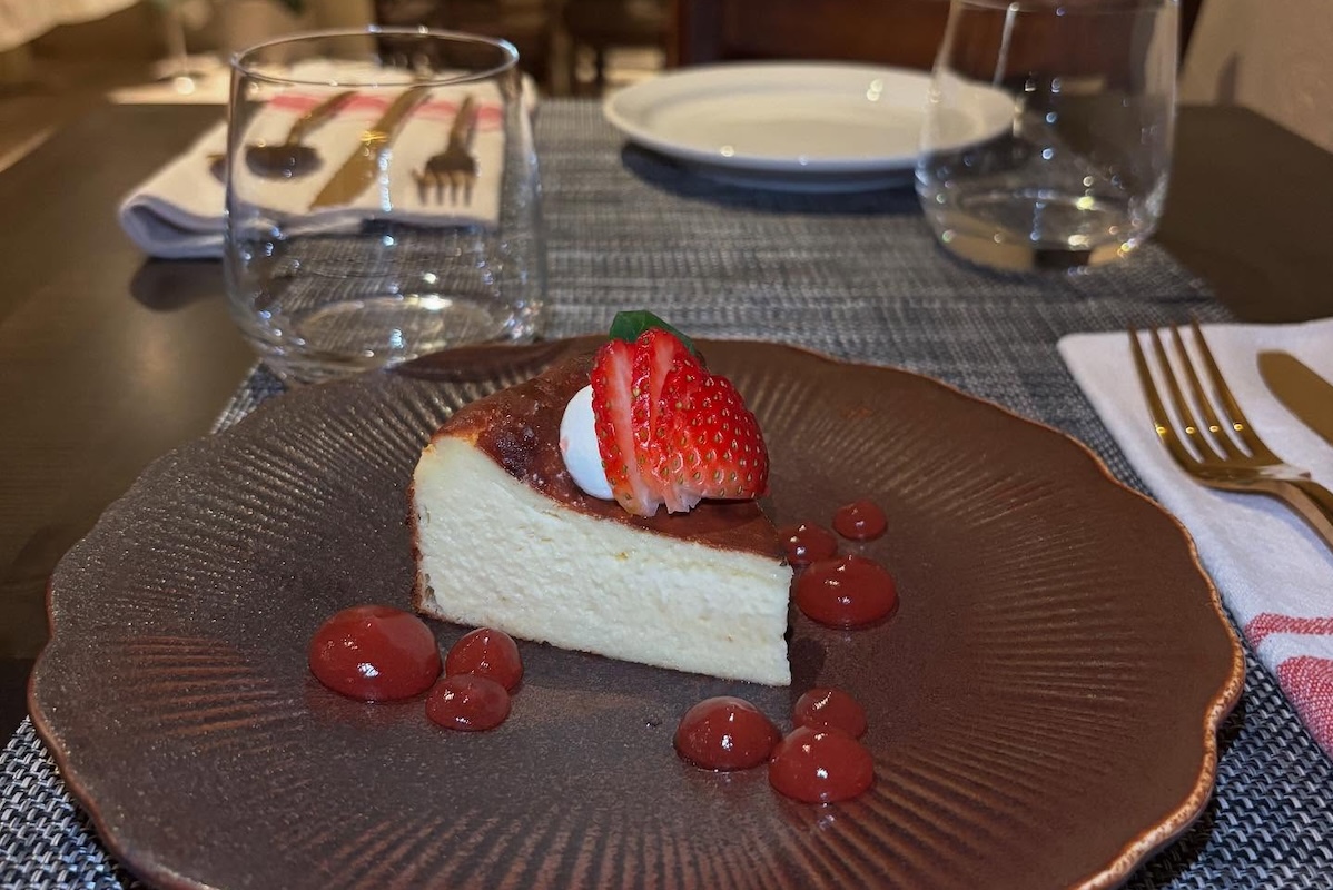 A plate with a slice of cheesecake topped with sliced strawberries. The plate is garnished with droplets of red jelly.