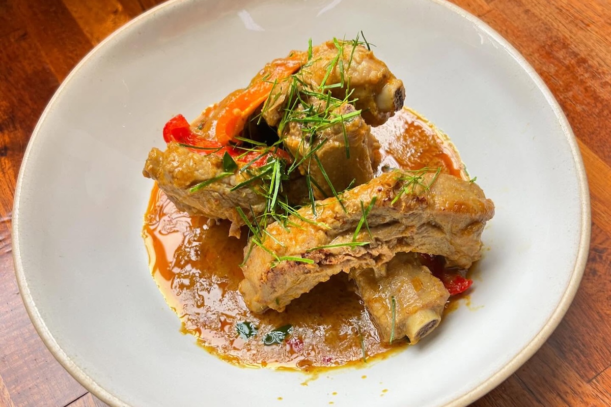 A plate with meat on the bone in a puddle of sauce and topped with herbs.