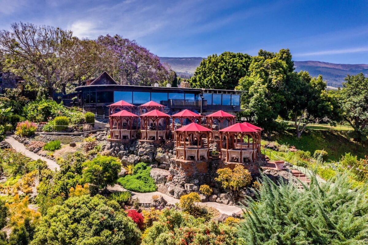 A hotel nestled in the side of a lush hill, complete with big windows and red umbrellas.