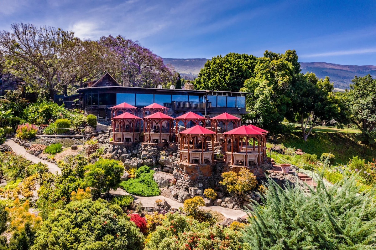 A hotel nestled in the side of a lush hill, complete with big windows and red umbrellas.