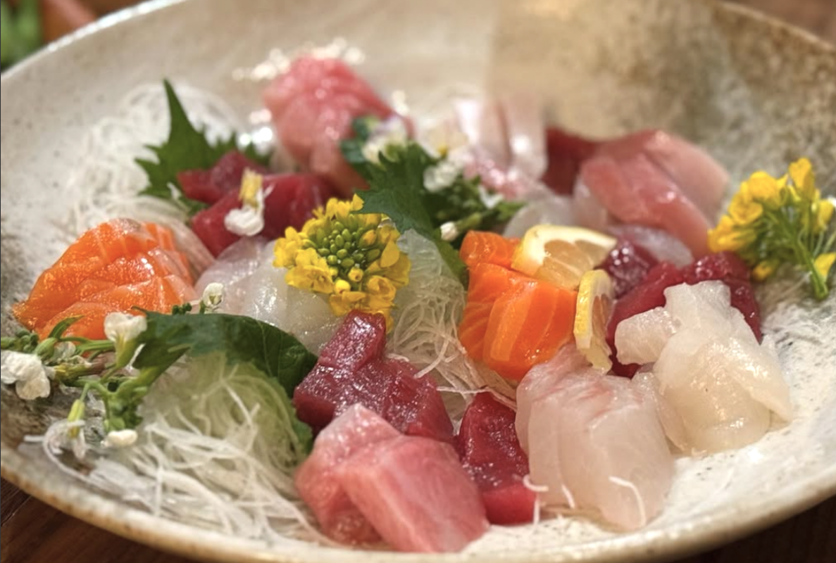 A plate with various cuts of fish, vermicelli noodles, citrus and edible flowers.