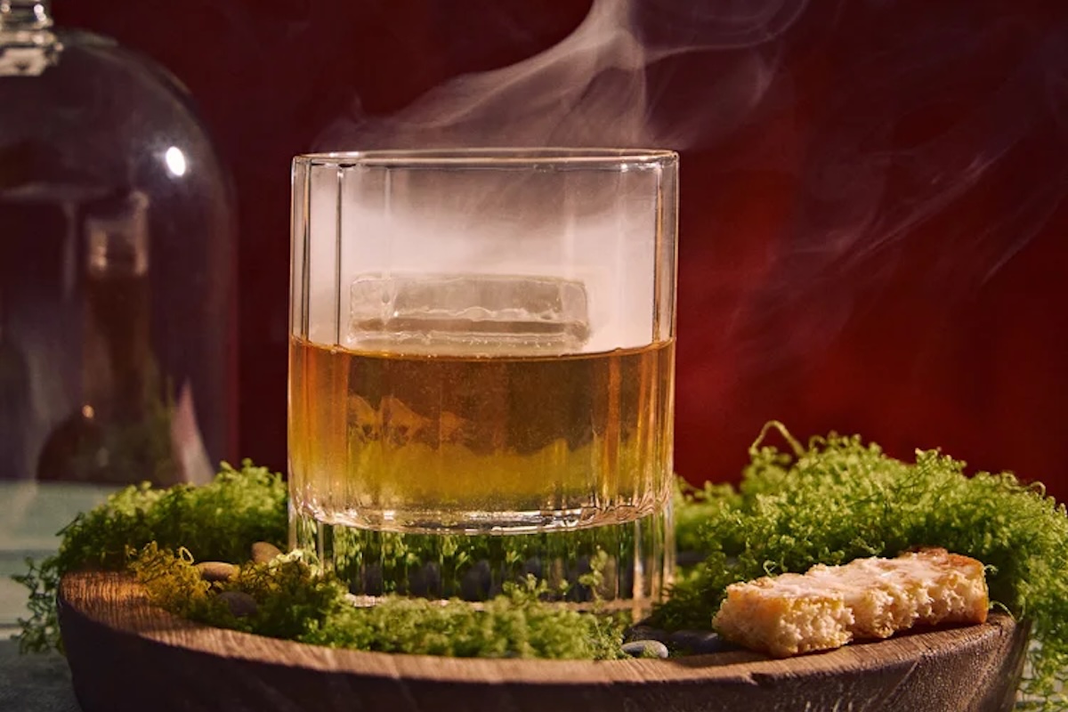 A cocktail with dry ice set on a wooden platter and surrounded by decorative moss.