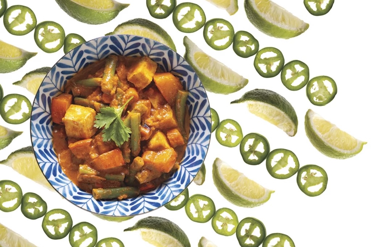 A bowl with tofu curry and a background pattern of lime and jalepeño slices.