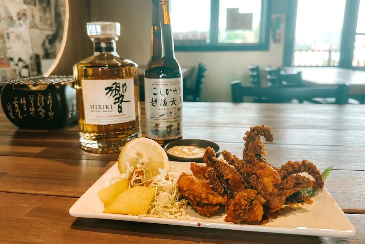 A plate with fried seafood and toppings and a couple of bottles of alcohol to the side.