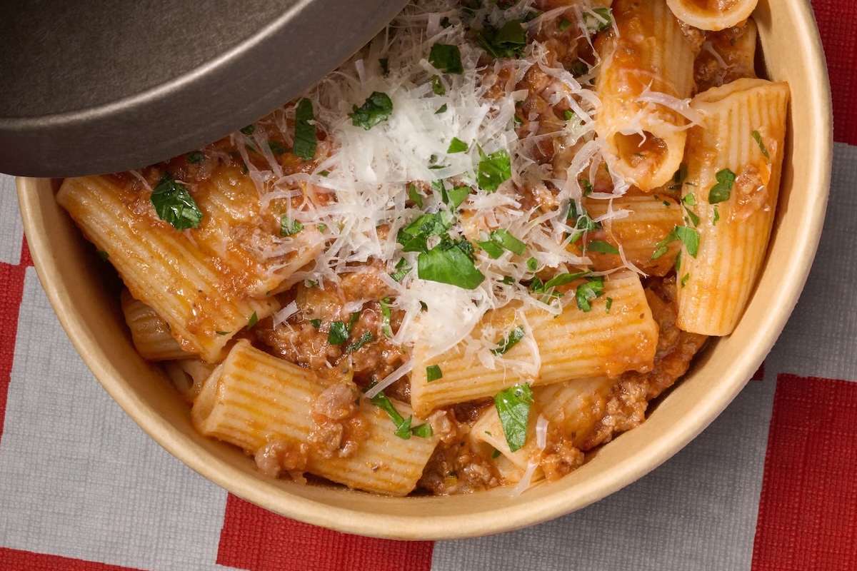 A bowl of rigatoni pasta with red sauce and topped with shredded parmesan and chopped herbs.