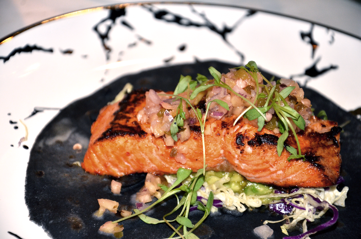 A marbled plate with grilled salmon topped with onions, tomatoes and microgreens.