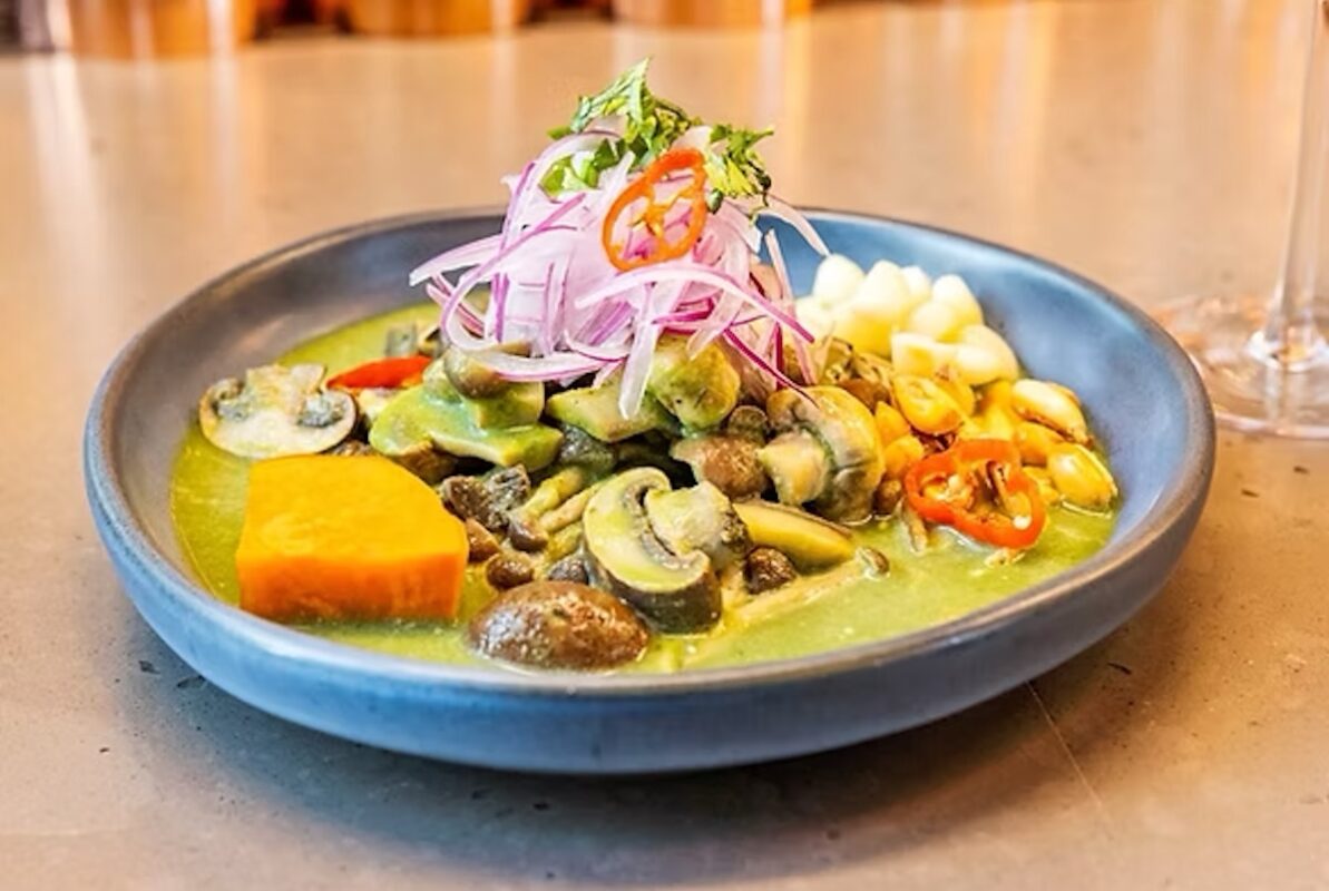 A blue plate with lots of veggies in sauce and topped with many garnishes.